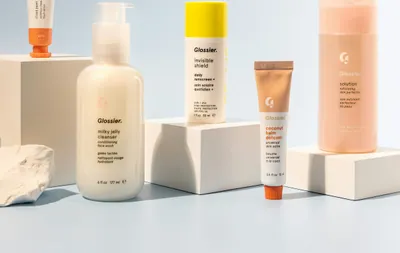 Assorted skincare products and a mascara wand arranged on white pedestals against blue