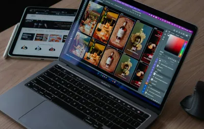 A laptop displaying photo editing software with a tablet and mouse on a wooden desk