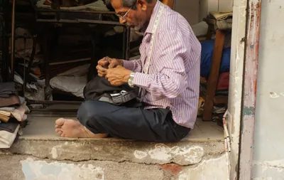 Barefoot tailor meticulously sewing clothes on a step